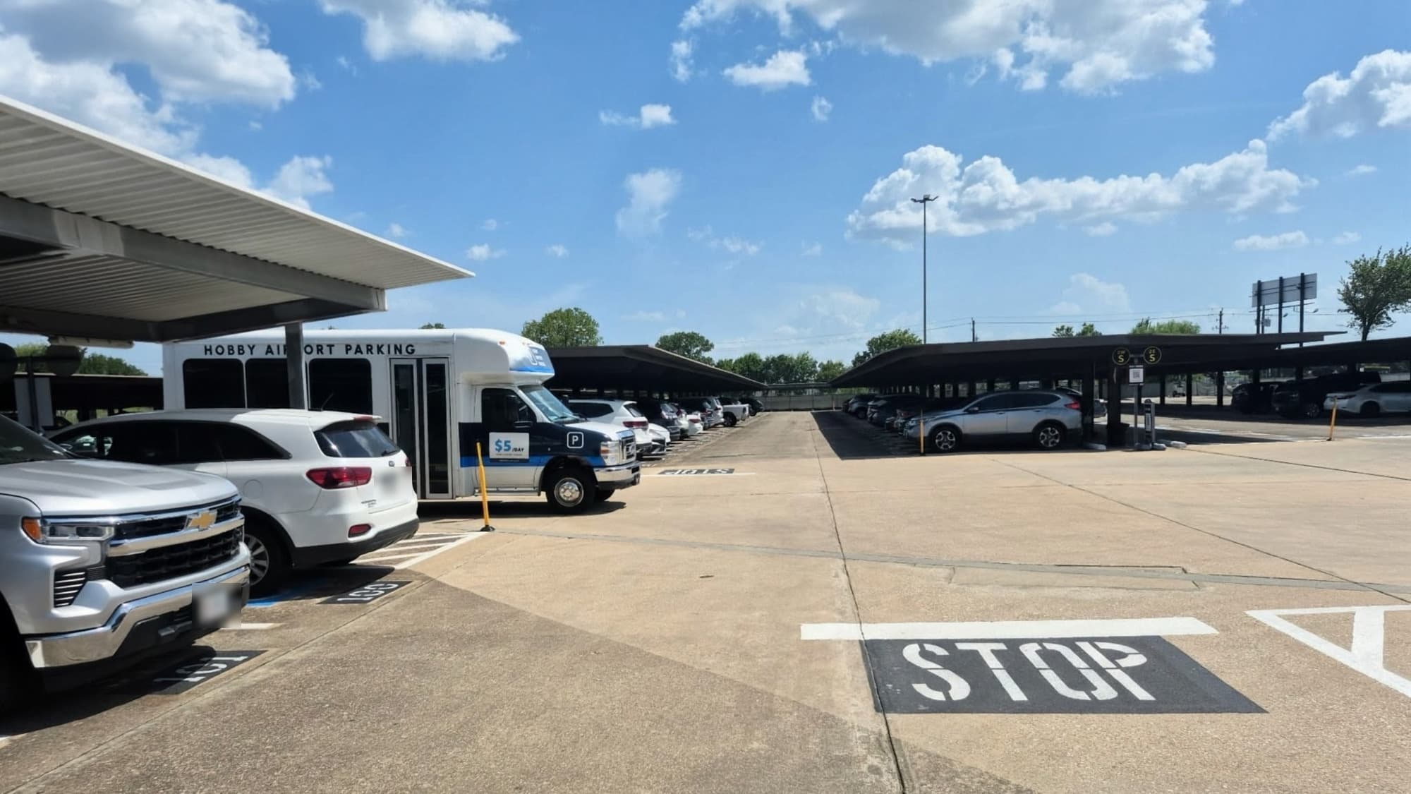 The Hobby Airport Parking shuttle waiting beside a covered parking row in the lot, where passengers board for the ride to the HOU terminal